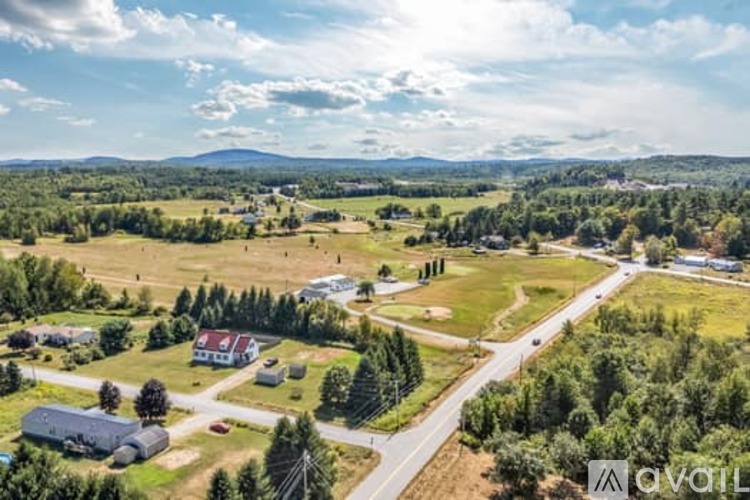 A rural landscape with a house, trees, and a road.