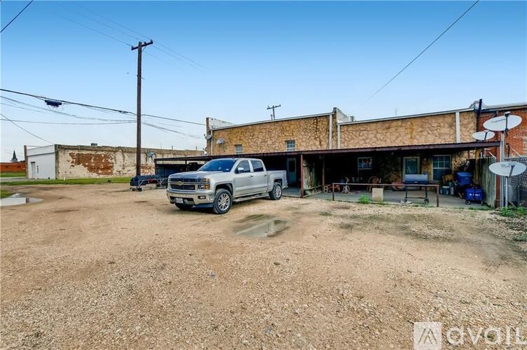 A silver truck is parked in front of a building with a dirt ground.