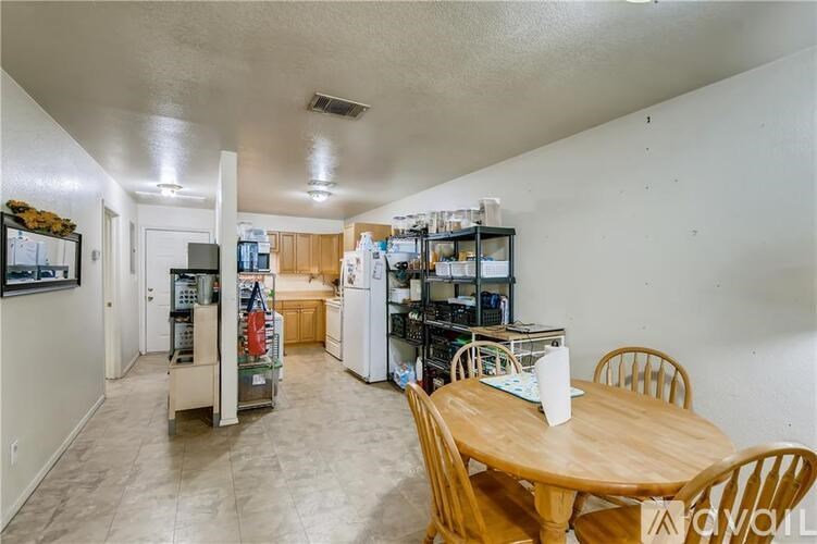 A kitchen with a table and chairs in the foreground and a refrigerator with a shelf of glasses on top.