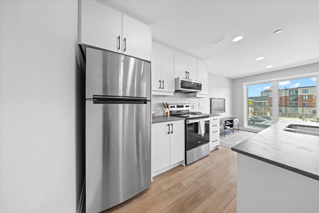 A modern kitchen with a stainless steel refrigerator and wooden flooring.