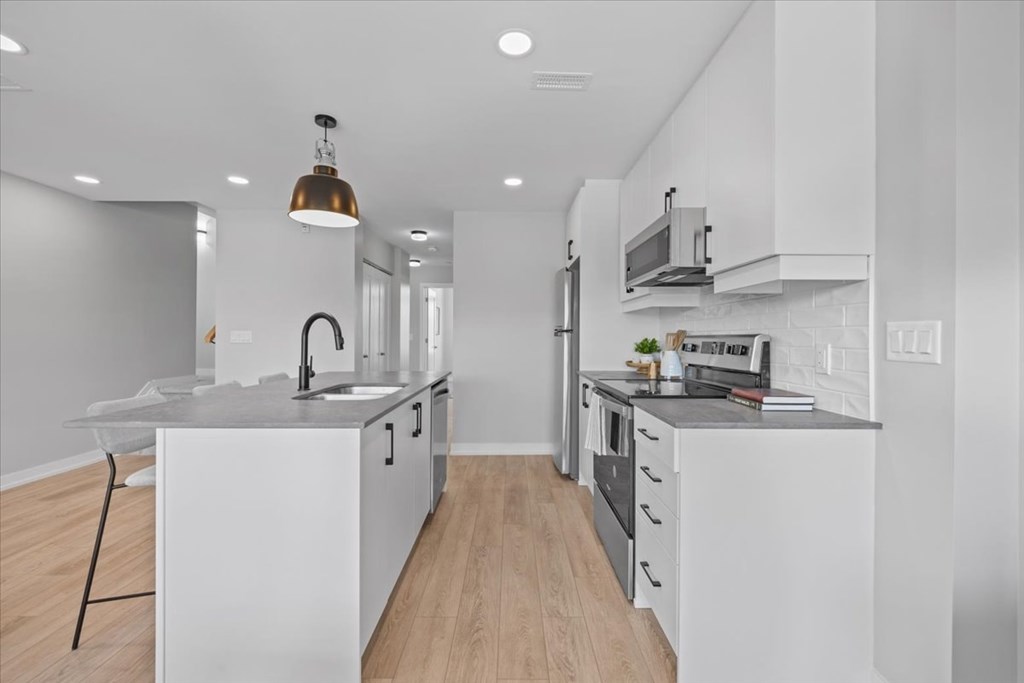 A modern kitchen with white cabinets and a wooden floor.