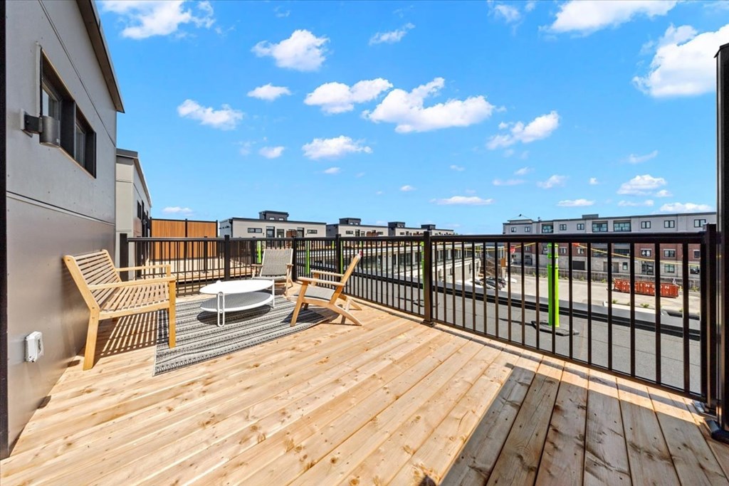A wooden deck with chairs and a table overlooking a city street.