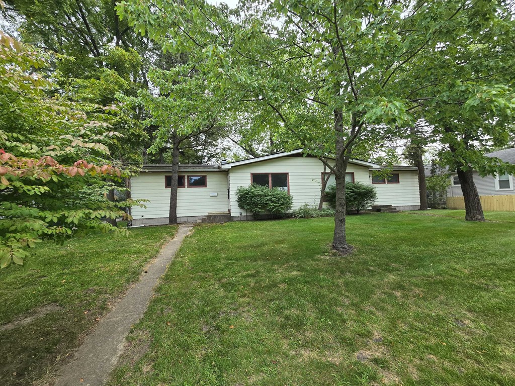 A house with a white exterior is surrounded by green trees and grass.