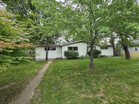 A house with a white exterior is surrounded by green trees and grass.