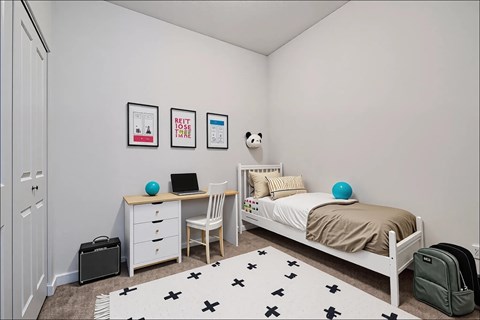 A bedroom with a bed, desk, chair, and a rug with black crosses on it.