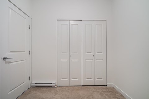 A white door is open to a room with a carpeted floor and a white wall.