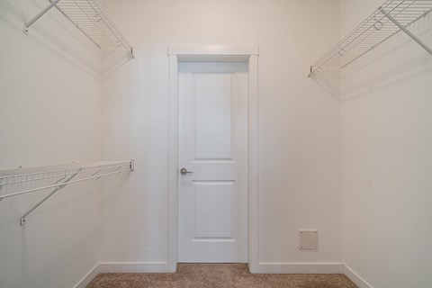 A white door is in the middle of a white room with a carpet on the floor.