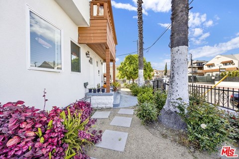 A white house with a wooden balcony and a palm tree in front.