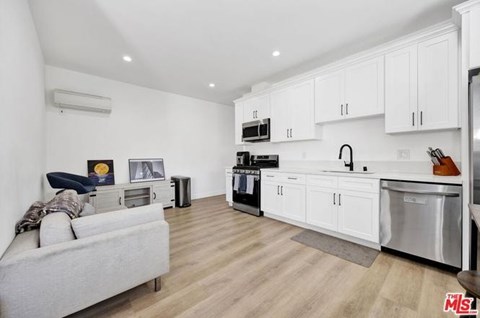 A kitchen with white cabinets and a grey couch.