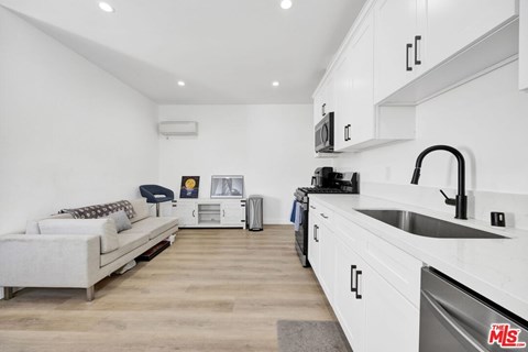 A modern kitchen with white cabinets and a white sofa with a cushion.