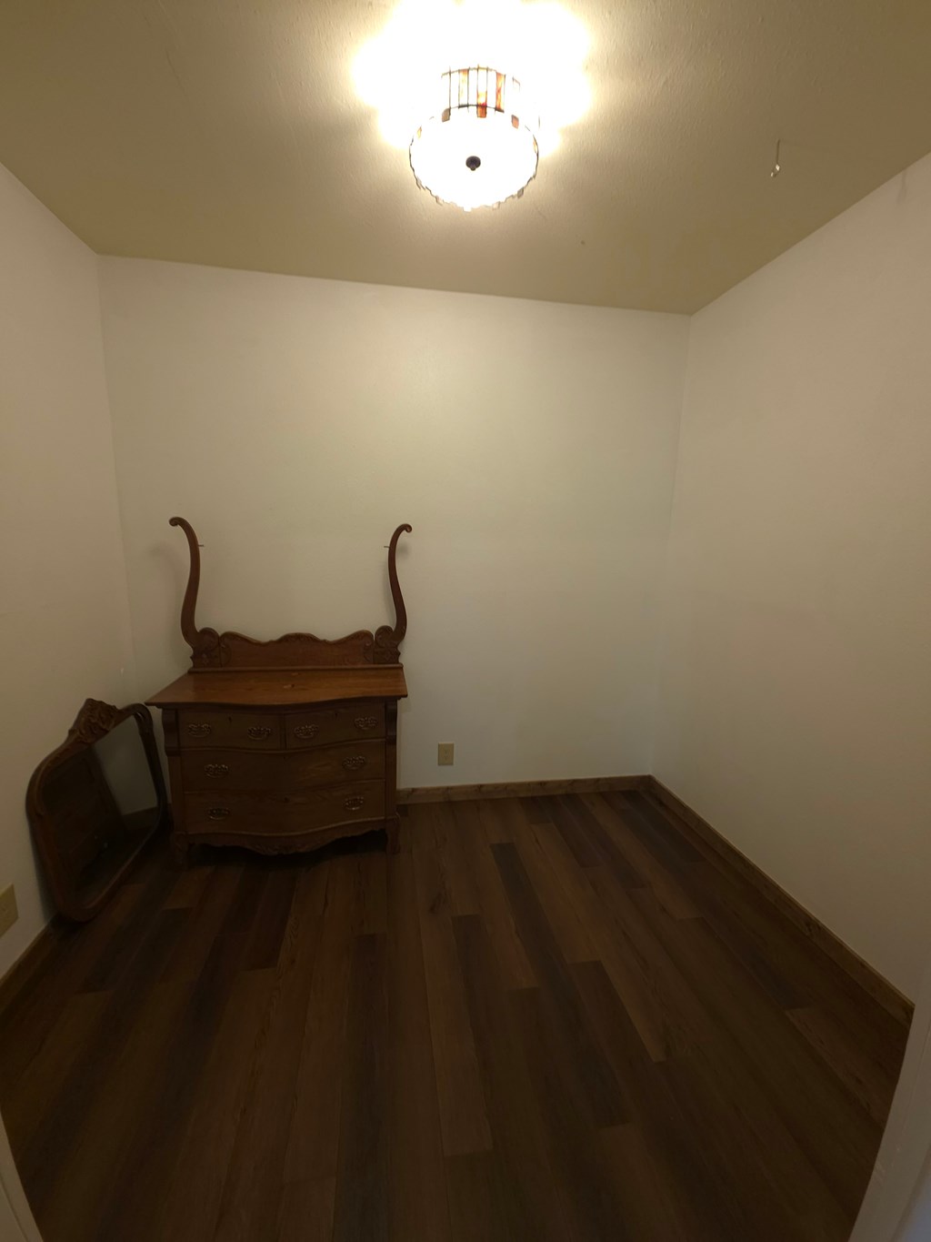 A room with a wooden floor and a brown bench under a light fixture.