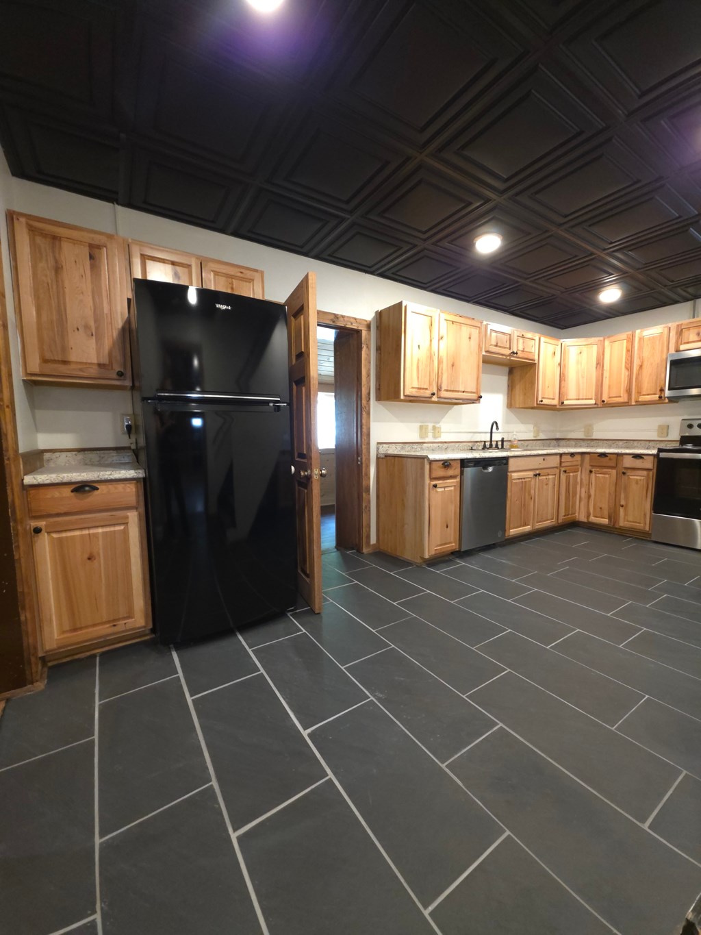 A black refrigerator in a kitchen with wooden cabinets.