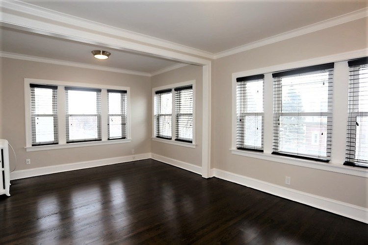 A room with wooden floors and three windows with blinds.