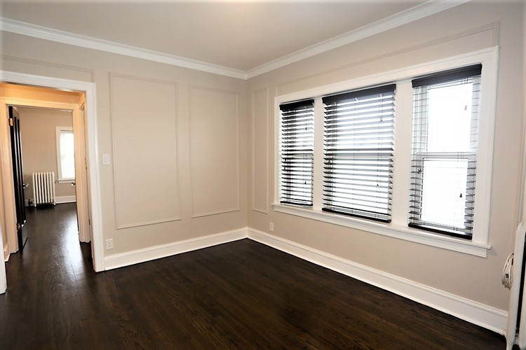 A room with wooden floors and two windows with blinds.