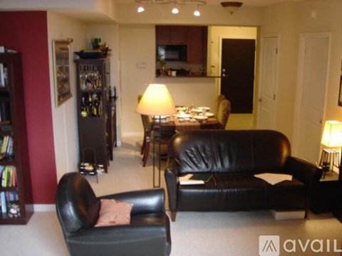 A black leather couch sits in a living room with a lamp and a bookshelf.