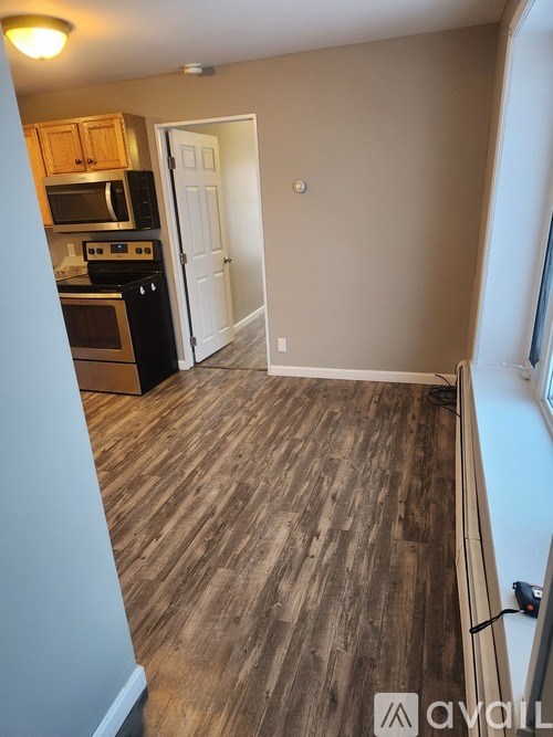 A room with wooden flooring and a kitchen area with cabinets and appliances.