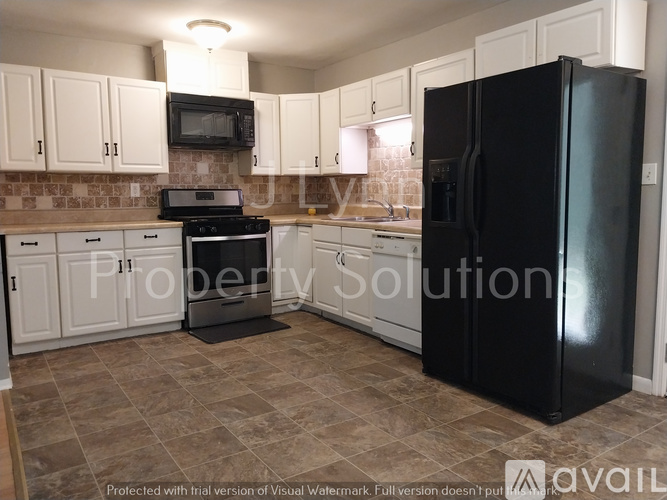 A black refrigerator in a kitchen with white cabinets.