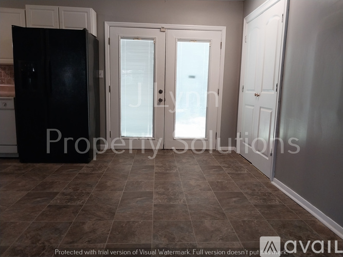 A kitchen with a black fridge, white cupboards, and a tiled floor.