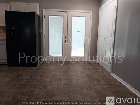 A kitchen with a black fridge, white cupboards, and a tiled floor.