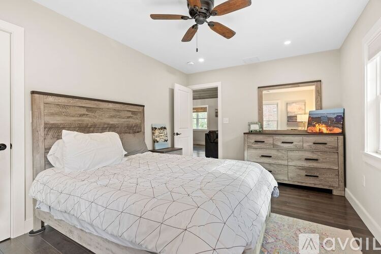 A bedroom with a large bed, a ceiling fan, and a dresser with a mirror above it.