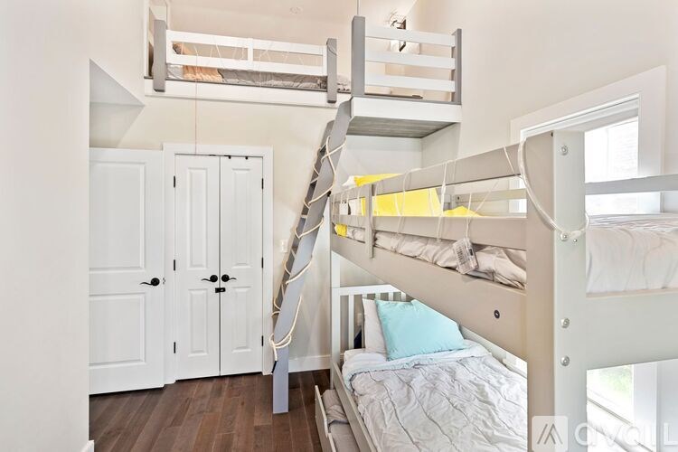 A white bunk bed with a ladder is in a room with a white door and a bed with a blue pillow.