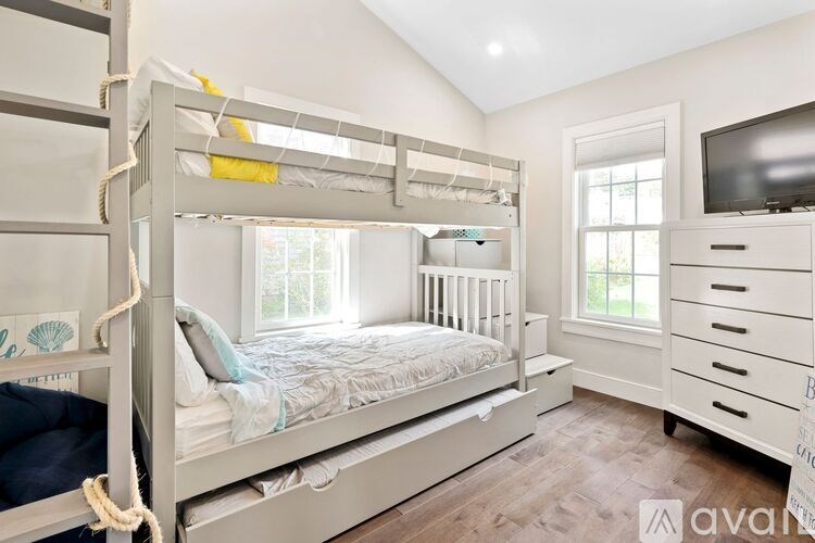 A white bunk bed with a rope ladder and a single bed with a white comforter.
