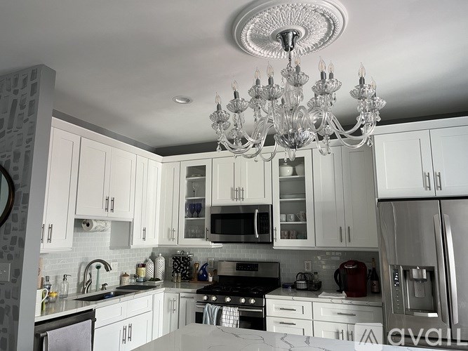 A chandelier hangs over a kitchen island with white cabinets and stainless steel appliances.