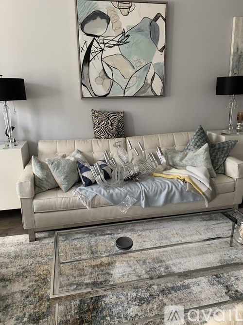 A grey couch with a grey blanket and pillows in front of a painting.