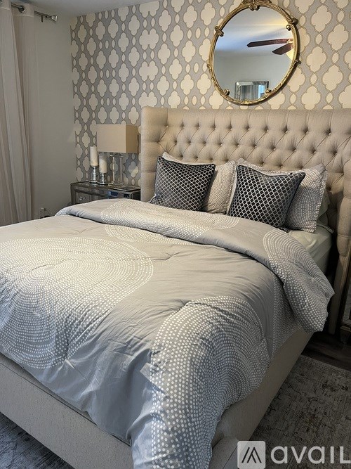 A bed with a white tufted headboard and a grey comforter is in the image.