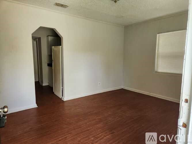 A room with wood flooring and a white wall with a doorway.