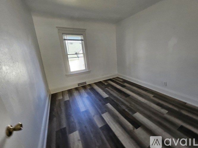 A room with wooden flooring and a window letting in sunlight.