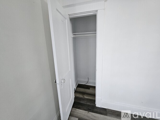 A white door is open to a small, empty room with a wooden floor.