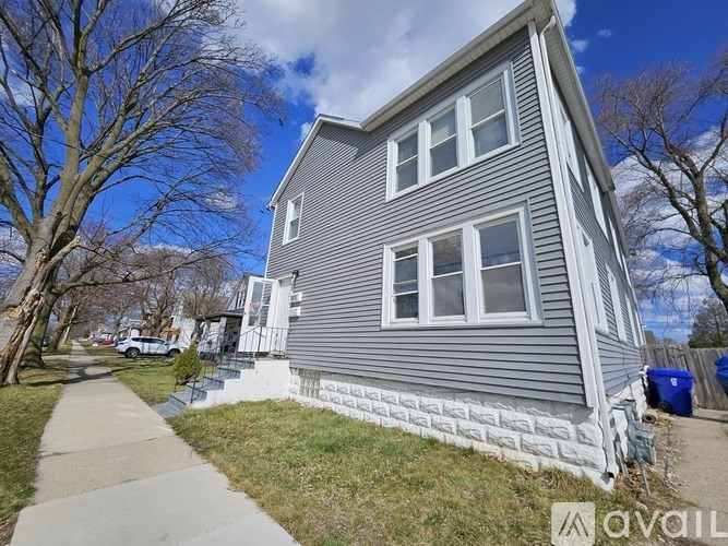 A grey house with a white fence and a blue trash can in front.