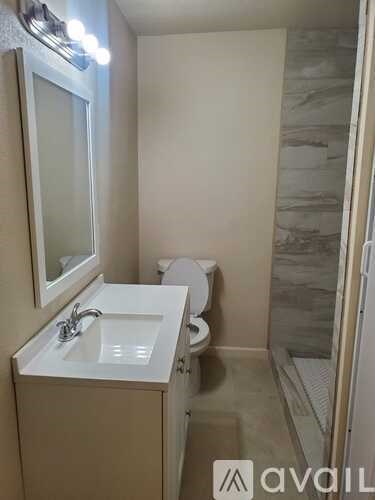 A bathroom with a toilet, sink, mirror, and a shower.