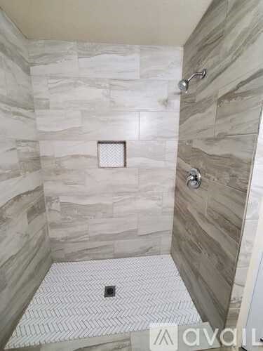 A shower with a marble wall and a white tiled floor.