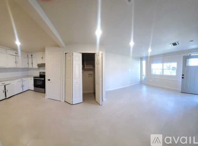 A spacious empty room with a kitchen area and a doorway leading to another room.