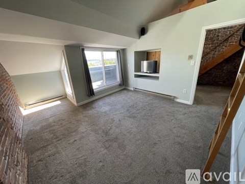 A living room with a grey carpet and a brick wall.