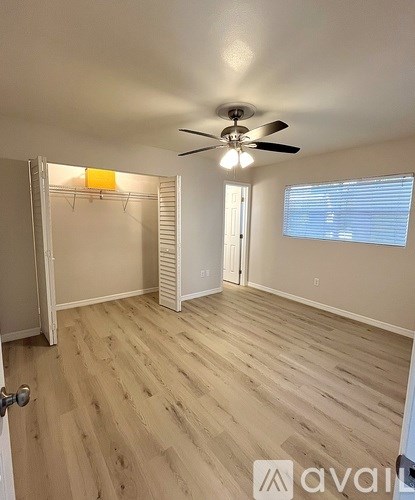 A room with a ceiling fan and light, wooden floors, and a door leading to another room.