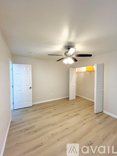 A room with a ceiling fan and light, hardwood floors, and a white door.