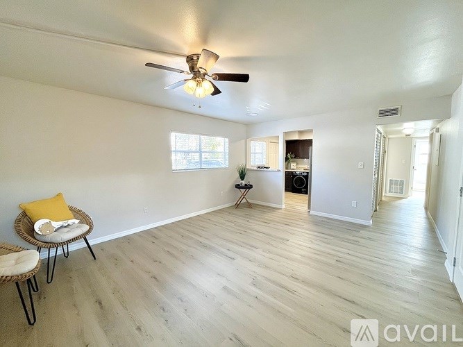 A spacious room with a ceiling fan and light, hardwood floors, and a window with a view.