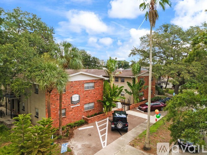 A red brick house with a white door and windows is surrounded by green trees.