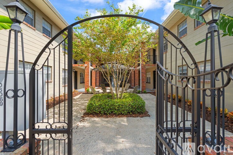 A black metal gate leads to a courtyard with a tree and a small bush.