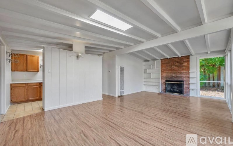 A spacious room with wooden floors and a brick fireplace.