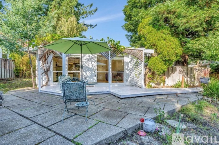 A patio with a table and chairs is surrounded by greenery.