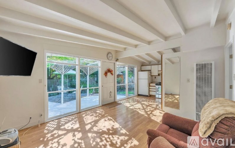 A living room with a couch and a rug in the foreground and a balcony with a table and chairs in the background.