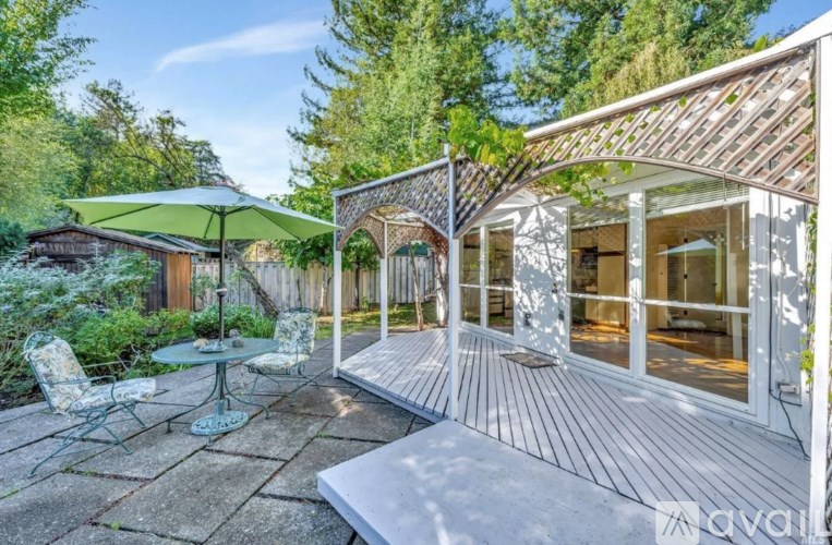A sunny day in a backyard with a white deck and a glass table.