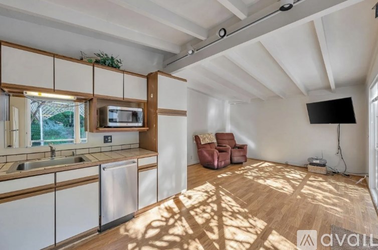 A sunlit kitchen with wooden floors and white walls.