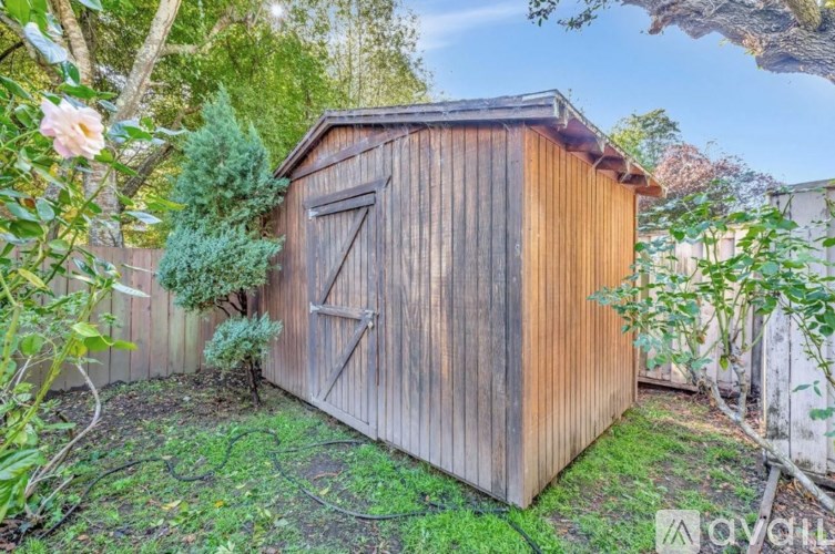 A wooden shed with a door and windows is surrounded by greenery.
