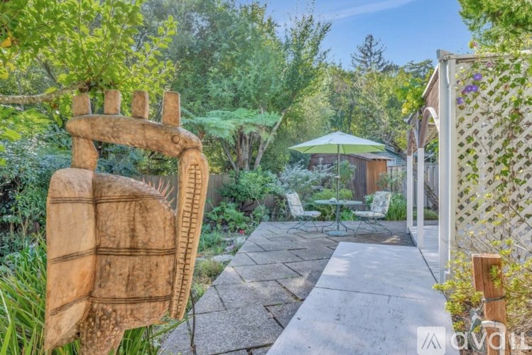 A garden with a stone pathway, a wooden sculpture, and a green umbrella.