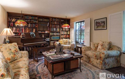 A living room with a piano, two chairs, a sofa, and a bookshelf filled with books.
